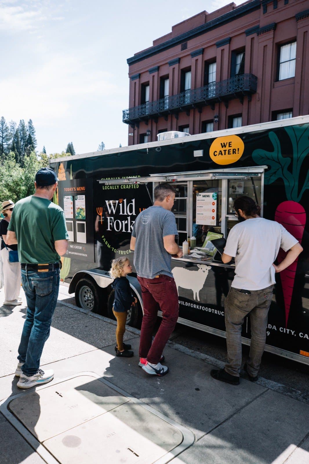 The Wild Fork food truck parked on a town street, with customers lined up at the order window.